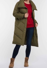Langer olivgrüner Daunenmantel mit einem gesteppten Design, hohem Kragen und Knopfverschluss, getragen über einem roten Pullover und dunklen Jeans.