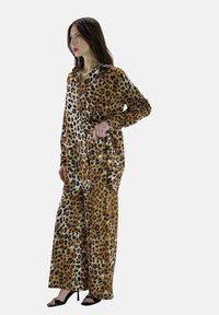 Monos con estampado de leopardo, de manga larga, piernas anchas y cuello. La tela presenta una mezcla de tonos marrones y blancos, creando un aspecto texturizado.
