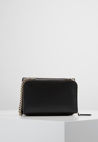 Sort læder crossover-taske med rektangulær form, guldkæde-strop og lynlåslukning. Glat tekstur med minimalistisk design.