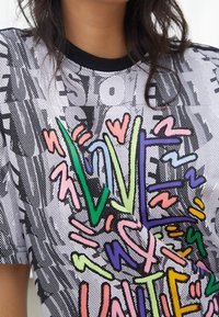 Lyhythihainen paita mustana, valkoisena ja värikkään graafisen kuvion kanssa, jossa on "LOVE" eloisissa, tyylitellyissä kirjaimissa teksturoidun taustan päällä.