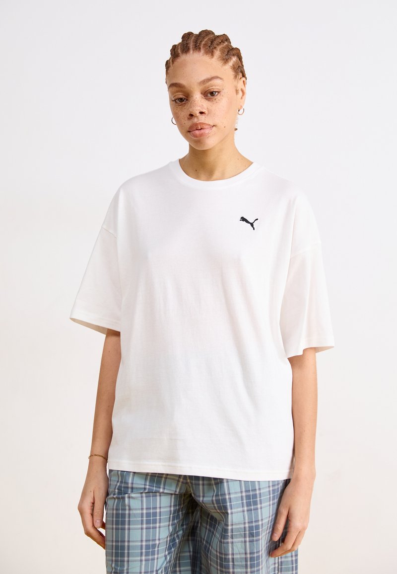 Tricou alb din bumbac, cu mâneci scurte, având un logo Puma negru pe partea stângă a pieptului. Este asociat cu pantaloni cu carouri albastre.