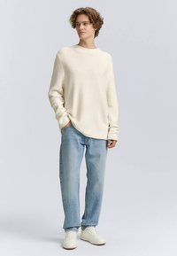 Pull en maille crème avec une texture côtelée, associé à un jean droit bleu clair et des baskets blanches. Design simple avec un col rond.