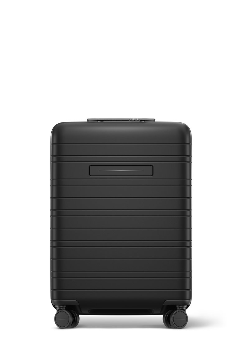 Valise rigide noire de forme rectangulaire, avec des stries verticales, une poignée rétractable et quatre roues pour la mobilité.