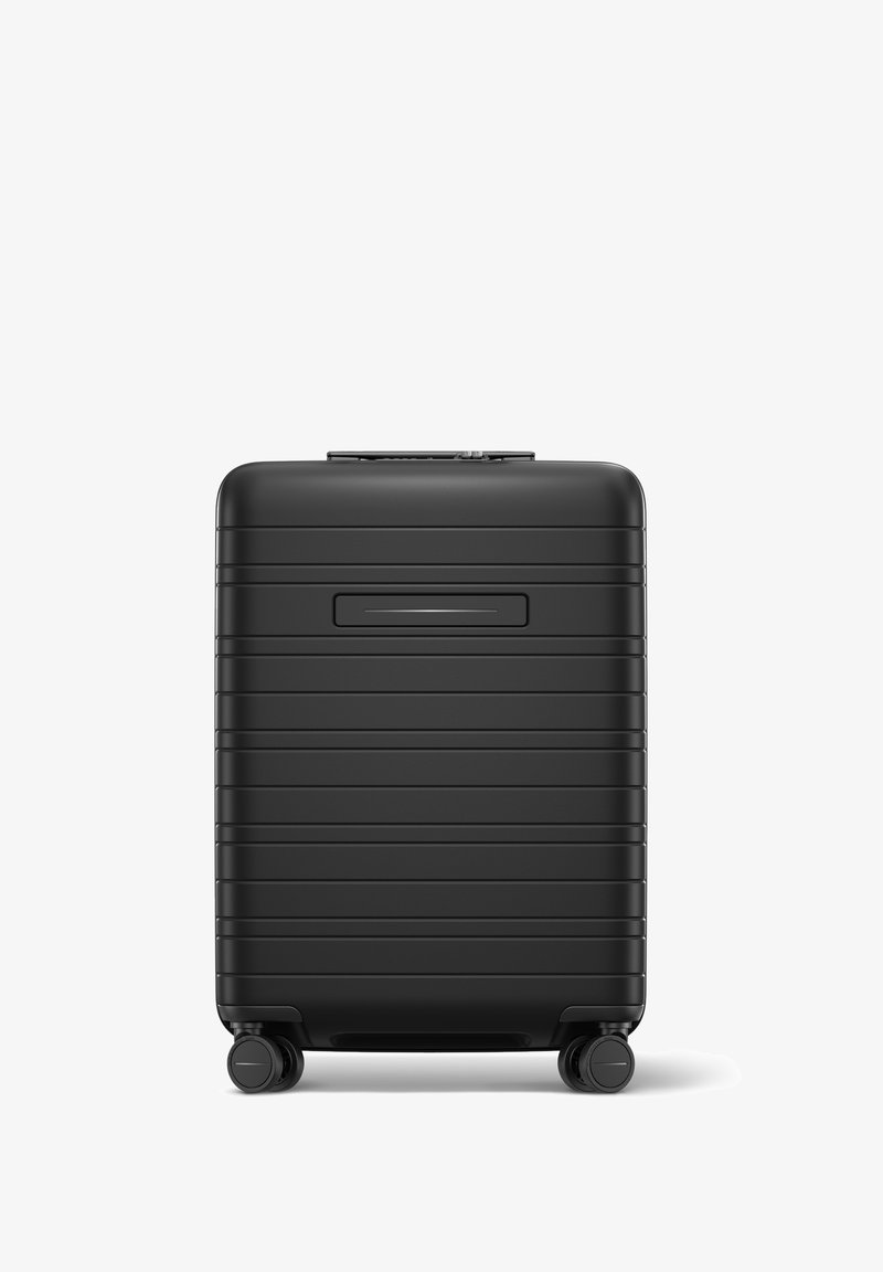 Valise rigide noire de forme rectangulaire, avec des stries verticales, une poignée rétractable et quatre roues pour la mobilité.