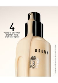 Beige flaske med svart pumpehode, med en logo med en krone og teksten "BROWN". Glatt tekstur og buet form, med væske synlig inni.