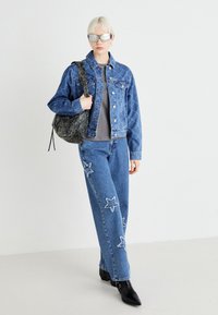 Denimska jakna z diamantskim vzorcem, siva majica, modri jeans z vezenimi zvezdami, črne gležnjarje in črna teksturirana torba.