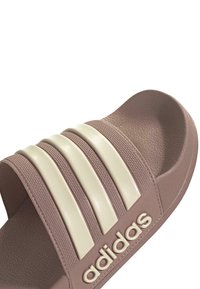 Roza klizna sandal s tri bijele horizontalne pruge na remenu, teksturirani vanjski materijal i urezani logo sa strane.