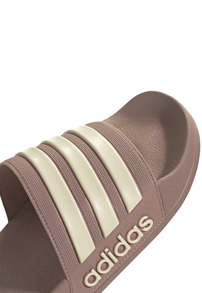 Rosa Rutschschuhsandale mit drei weißen horizontalen Streifen auf dem Riemen, strukturiertem Außenmaterial und geprägtem Logo an der Seite.
