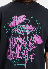 Camiseta negra con un diseño gráfico de formas botánicas en rosa y turquesa y círculos abstractos. Material de algodón suave, corte relajado.