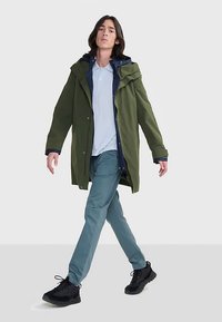 Maslinasto zelena parka s kapuljačom, s patentnim zatvaračem i gumbima. Nošena preko svijetloplave polo majice i svijetloplavih hlača, uparena s crnim tenisicama.