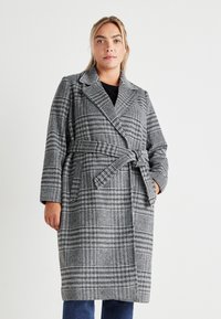 Μακρύ καρό παλτό σε μαύρο και λευκό, με διπλό κούμπωμα, μεγάλο γιακά και ζώνη που δένει στη μέση. Μαλακή υφή υφάσματος.