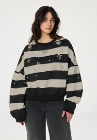 Zwart en beige gestreepte sweatshirt met versieringen, waaronder kralen en decoratieve elementen, met een ontspannen pasvorm en ribgebreide manchetten.