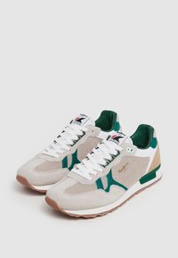 Sneaker con superiore in mesh e suede grigio chiaro con dettagli verdi, lacci bianchi e suola in gomma marrone. Include un logo sul lato.