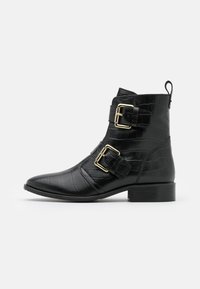 Botas negras hasta el tobillo hechas de cuero con relieve de cocodrilo, que cuentan con dos hebillas doradas, puntera afilada y un tacón bajo.