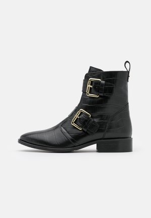 Czarne botki za kostkę z tłoczonej skóry jak krokodyl, z dwoma złotymi klamrami, spiczastym noskiem i niskim obcasem w kształcie kostki.