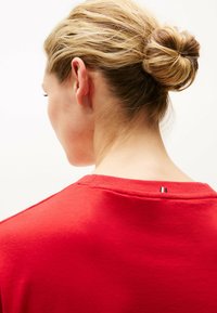 Rotes Baumwoll-T-Shirt mit rundem Ausschnitt und kurzen Ärmeln. Rückansicht zeigt ein kleines dreifarbiges Etikett am Nacken. Weiche Textur.