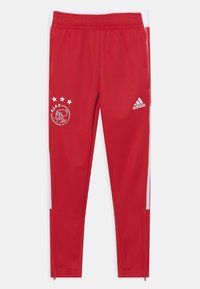 Czerwone spodnie sportowe wykonane z gładkiej tkaniny z białymi paskami po bokach. Posiadają logo klubu i cztery gwiazdki nad nim oraz zamki błyskawiczne przy kostkach.