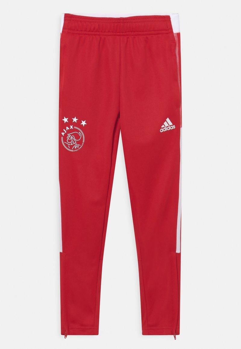 Czerwone spodnie sportowe wykonane z gładkiej tkaniny z białymi paskami po bokach. Posiadają logo klubu i cztery gwiazdki nad nim oraz zamki błyskawiczne przy kostkach.