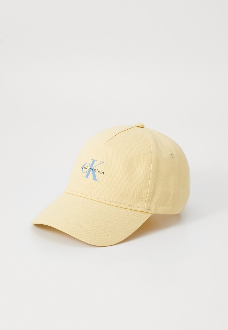 Casquette de baseball jaune clair avec visière incurvée, avec le logo "CK Calvin Klein" bleu clair sur le panneau avant, sur fond blanc.