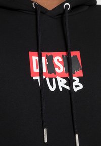 Svart hoodie med dragsko, med en grafisk design i röd och vit text som säger "DISRUPT." Mjuk textur, avslappnad passform.