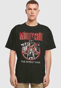 Sort bomulds T-shirt med et rødt og hvidt grafisk tryk af bandmedlemmerne foran et pentagram, med tekst der siger "MÖTLEY CRÜE THE WORLD TOUR."