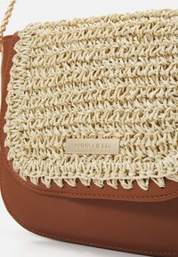 Borsa in pelle marrone con pattina intrecciata beige e placca dorata incisa "Anna Field," dotata di tracolla in catena dorata.