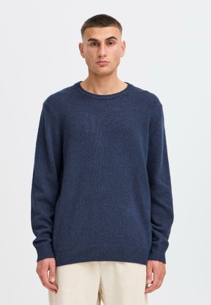 Pull en maille bleu marine avec des manches longues, un col rond et des bords côtelés. Texture douce avec une coupe légèrement ample.