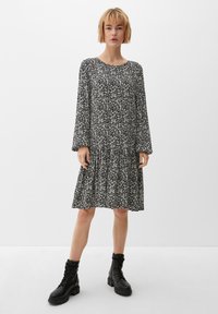 Schwarzes und weißes Blumenkleid mit langen Ärmeln, gerafftem Bund und gestuftem Rock. Getragen mit schwarzen Stiefeln im Combat-Stil. Glatte Stoffstruktur.