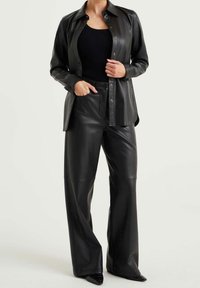 Svart konstläder skjorta med knappar i kombination med matchande vida byxor. Outfiten har en strukturerad ribbvävd topp under.