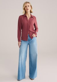 Camisa abotonada color granate con mangas largas, combinada con jeans de pierna ancha en azul claro. Textura de tela lisa y ajuste entallado.