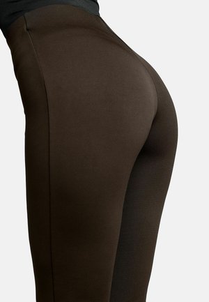 Primo piano di una persona che indossa pantaloni aderenti marrone scuro che evidenziano il tessuto avvolgente intorno all'area dell'anca e della coscia.