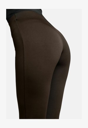 Približan prikaz osobe koja nosi uske tamno smeđe hlače, ističući prilagođenu tkaninu oko bokova i bedara.