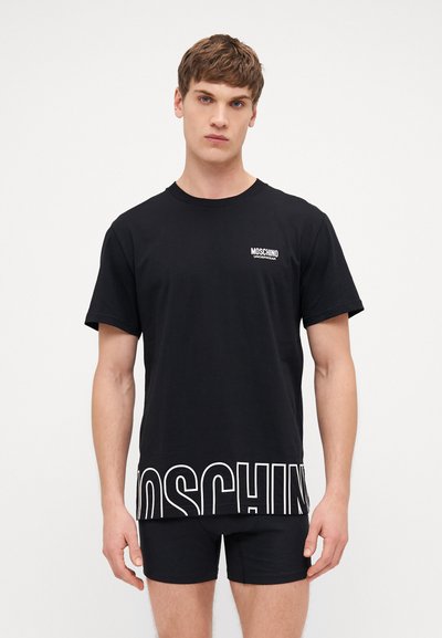 T-shirt nera in cotone con maniche corte, caratterizzata da un logo bianco "MOSCHINO" sul petto e grande lettering bianco lungo l'orlo.
