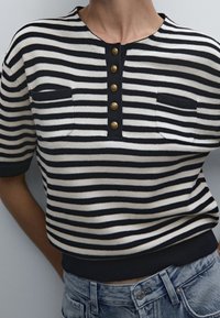 Randig stickad topp i marinblått och vitt, med rund halsringning, korta ärmar, guldfärgad knapplist och två bröstfickor.