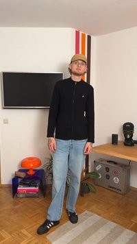 Schwarze, enganliegende Strickjacke mit langen Ärmeln und rundem Kragen, kombiniert mit hellblauen, geraden Jeans und schwarzen Sneakers mit weißen Streifen.