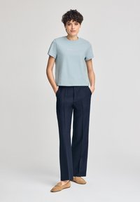 Ljusblå bomullströja med korta ärmar och rundad halsringning, ihopparad med marinblå vida byxor och beige mockaskor utan snörning.