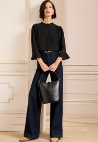 Black blouse with scalloped neckline and ruffled sleeves, paired with dark denim wide-leg pants and a structured black leather handbag.