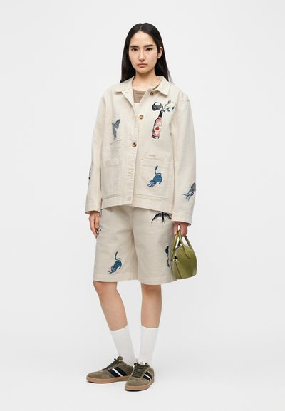 Μπεζ κεντημένο μπουφάν με διάφορα σχέδια, ταιριαστό σορτς και πράσινη τσάντα χειρός. Διαθέτει κούμπωμα με κουμπιά και κοντά μανίκια. Καφέ αθλητικά παπούτσια.