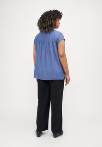 Blue short-sleeve blouse with pleated back detail, soft texture, worn with black wide-leg pants and black shoes.