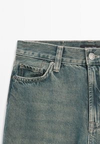 Blue denim jeans with a classic five-pocket design, featuring a faded texture, contrasting stitching, and a metal button closure.
