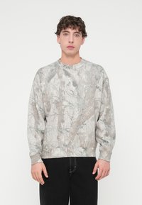 Γκρι φούτερ με καμουφλάζ μοτίβο σε διάφορες υφές και αποχρώσεις. Ριμπ μανσέτες και τελείωμα, άνετη γραμμή, στρογγυλή λαιμόκοψη.