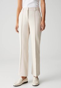 Beige op maat gemaakte broek met een hoge taille, scherpe plooien en wijde pijpen. Gemaakt van een gladde stof, gestyled met een subtiele glans en zijzakken.