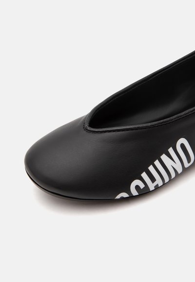 Chaussure plate noire avec bout arrondi et nom partiel de la marque « MOSCHINO » imprimé sur le côté.