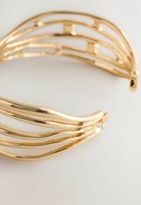 Bracelet en or avec des brins courbés et ondulés. Il présente une surface polie avec une finition brillante et une texture lisse.