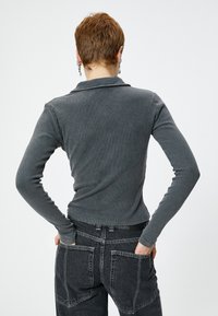 Grå ribbet langærmet polo med krave, båret med mørke jeans med store baglommer. Tæt siddende design.