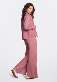 Conjunto de denim rosa claro que incluye una chaqueta de manga larga y pantalones de pierna ancha. El material tiene una textura suave con costuras visibles y bolsillos.