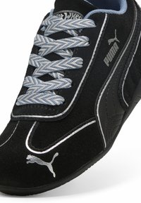 Črne semiš športne superge s srebrnimi poudarki, modrimi vezalkami in izrazitim logotipom Puma. Imajo aerodinamičen dizajn in teksturiran stranski panel.