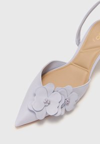 Chaussure pointue lavande clair avec un design à talon ouvert, ornée de superpositions de fleurs et d'une finition mate. Semelle intérieure douce.