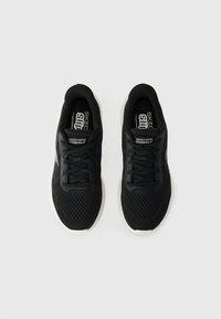 Mustat urheilukengät verkkomateriaalista, nauhalla suljettavalla designillä, valkoisella pehmeällä ulkopohjalla ja "SKECHERS GOWALK" -brändäyksellä kielekkeessä.