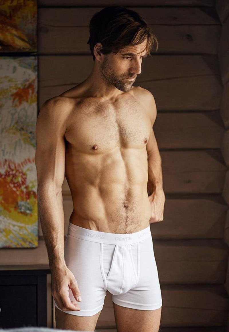 Hvide bomuldsboxershorts med en blød talje, der pryder mærkenavnet "DOVRE." Modellen har en muskuløsbygning og kort hår.